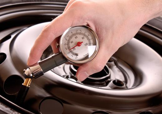 A man checks the pressure in a car tire, without removing the hubcap.